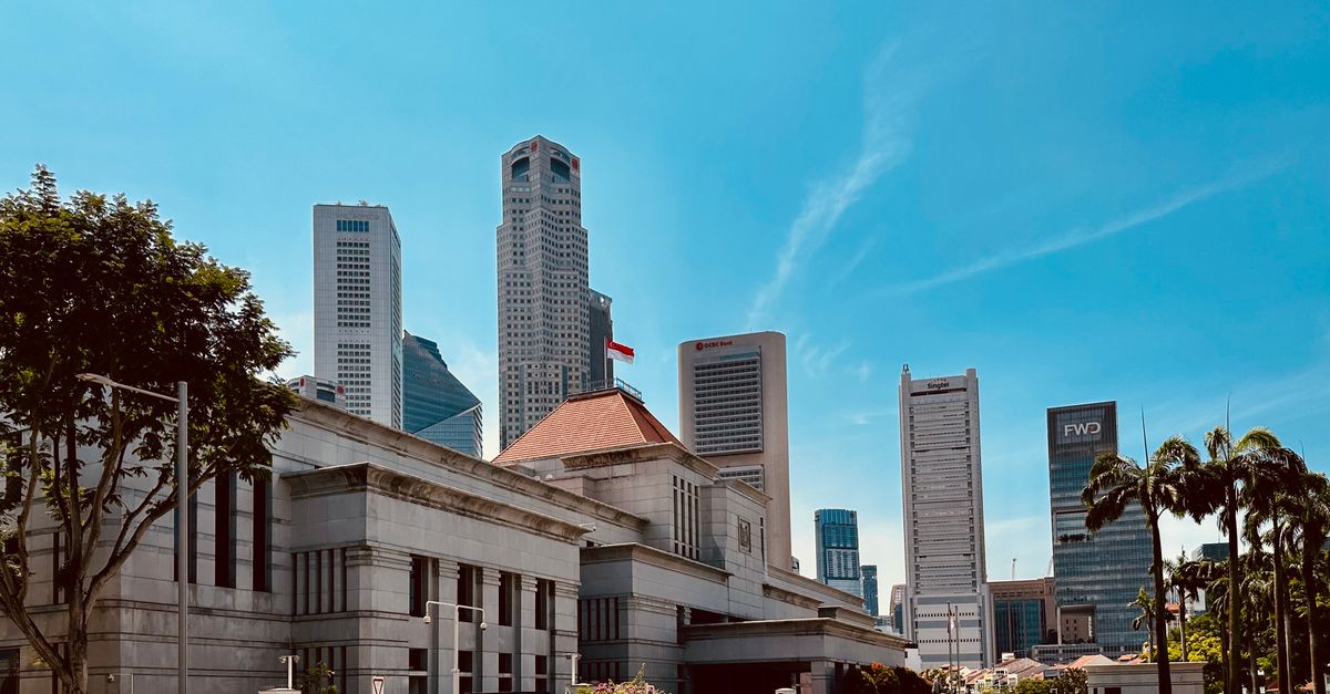 Bâtiment officiel au toit de tuiles surmonté du drapeau de Singapour, devant les tours du quartier d’affaires