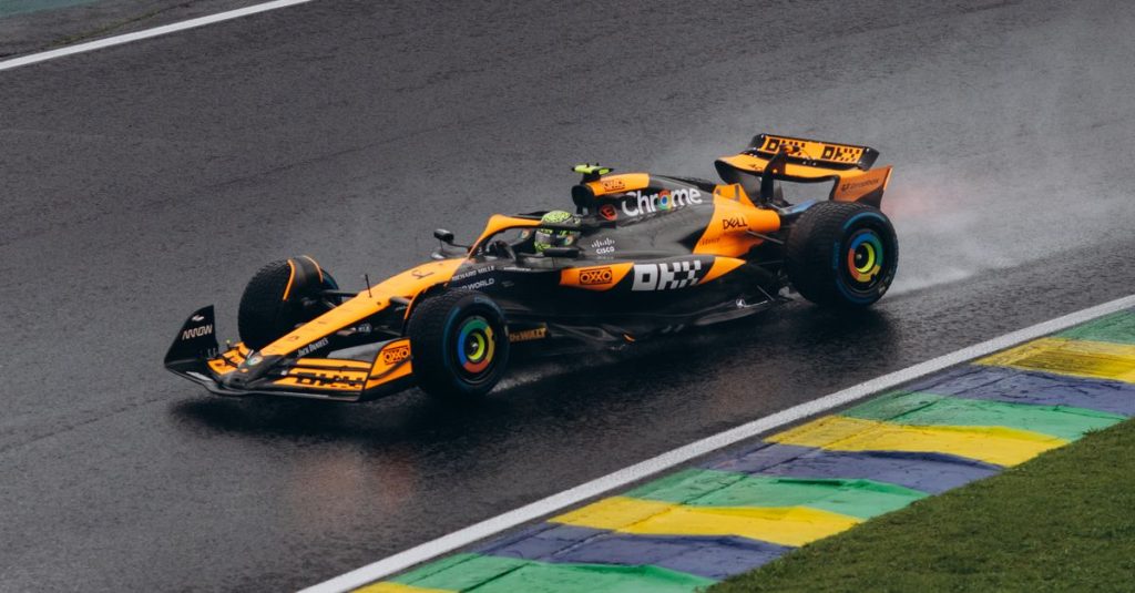Monoplace de Formule 1 orange sur une piste mouillée, devant des vibreurs colorés